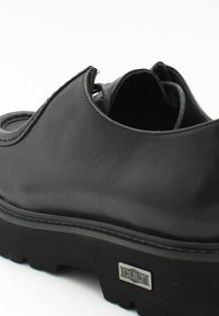 Chaussure en cuir noir avec un design arrondi, surface texturée, embout et talon renforcés, et une semelle crantée contrastante. Présente un branding subtil.