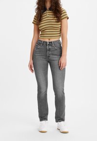 Pantalones vaqueros grises de cintura alta con pierna recta, combinados con una camiseta tipo polo de rayas amarillas y azul marino de manga corta, y calzados con zapatillas blancas.