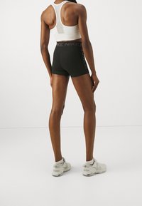 Czarne sportowe spodenki z wysokim stanem z logo „Nike”, noszone z białym biustonoszem sportowym i jasnoszarymi trampkami. Gładka faktura.