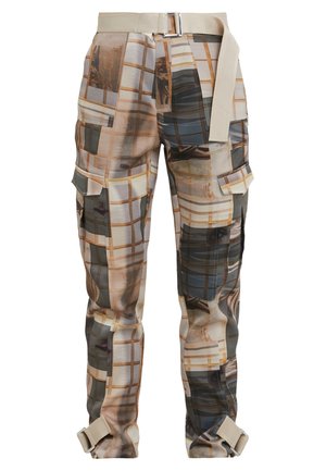 Henkilö seisoo yllään beige ylisuurikokoinen takki, valkoinen ribbineulottu toppi, kuvioidut cargo-housut vyöllä ja kermaan vivahtavat vaelluskengät mustilla nauhoilla.