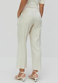 Lichtbeige linnen broek met een brede pijp, elastische tailleband en zijzakken, gecombineerd met witte sandalen met hoge hakken en bandjes.