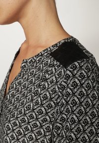 Chemisier noir et blanc à motifs présentant un design géométrique, avec un détail texturé aux épaules noires et un col rond.
