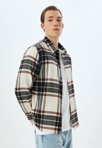 Geruite flanellen shirt in crème, zwart en bruin. Heeft een knoopsluiting aan de voorkant, een klassieke kraag en lange mouwen met een relaxte pasvorm.