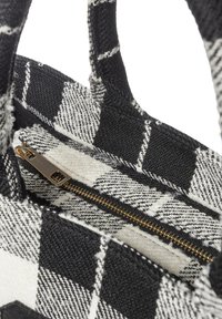 Zwart-wit geruite stoffen handtas met een textuurafwerking, voorzien van gouden ritssluitingen en twee geweven handvatten.