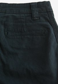 Poche arrière du pantalon bleu marine foncé avec un passepoil unique, une boucle de ceinture et des coutures visibles sur tissu en coton.