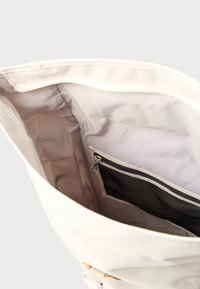 Unutrašnjost bijele torbe za nošenje s glatkom tkaninom, sadrži džep na patentni zatvarač i pretinac od mrežice. Dizajn je jednostavan i funkcionalan.