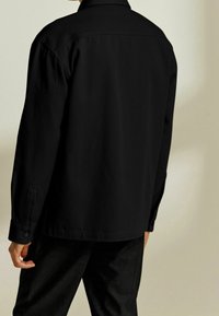 Zwart shirt met lange mouwen, een kraag, knoopmanchetten en een rechte snit, met een gladde, matte stoffen textuur.