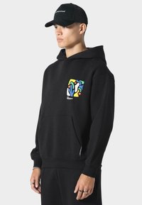 Sudadera negra de algodón, con un diseño abstracto colorido en el lado izquierdo del pecho. Incluye un bolsillo frontal y un corte holgado.