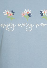 Vaaleansininen t-paita, jossa on kukkakuosi, valkoisia päivänkakkaroita, vaaleanpunaisia ja sinisiä kukkia sekä vihreitä lehtiä, ja tekstinä "nauti joka hetkestä."