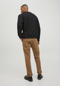 Schwarzes Baumwoll-Sweatshirt mit Rundhalsausschnitt, kombiniert mit hellbraunen Baumwollhosen. Die Hosen haben aufgeschlagene Säume und zwei Gesäßtaschen.
