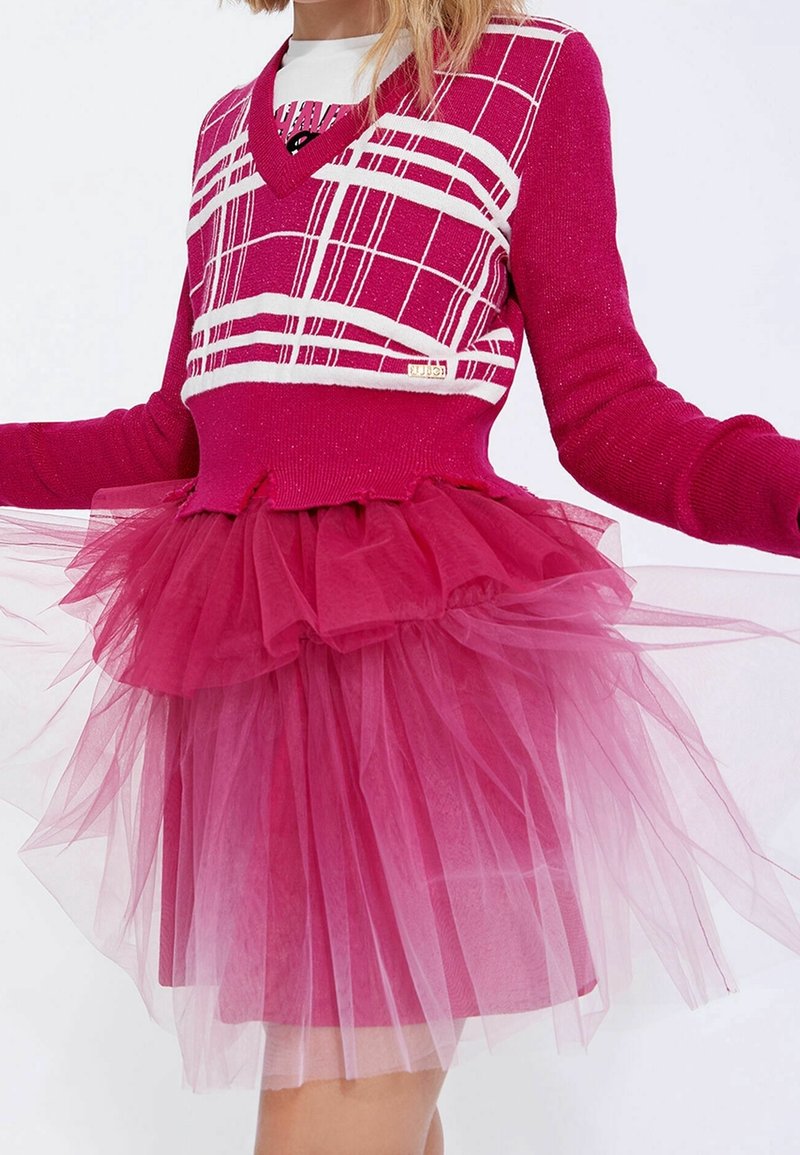 Pull en tricot fuchsia avec un motif à carreaux blancs et un col en V, associé à une jupe en tulle superposée d'un rose assorti avec une texture duveteuse.
