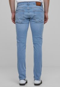 Világoskék farmernadrág, slim fit fazonban, bőrszíjjal a derékpánton és két hátsó zsebbel. Sima tapintás és klasszikus dizájn.