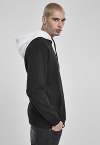 Fekete kapucnis pulóver fehér csíkos kapucnival, puha anyagból készült. Elöl zsebe van és állítható zsinórral rendelkezik. Simább textúra, laza fazon.