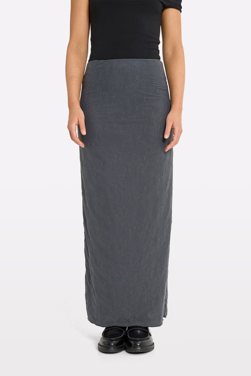 Maxihame made of dark gray fabric with floral embroidery, fitted at the waist, smooth texture, paired with black shoes.