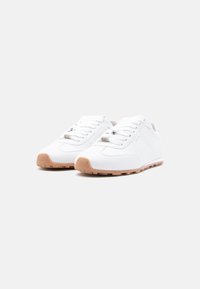 Paire de baskets en cuir blanc avec des lacets blancs et des semelles en caoutchouc brun clair sur un fond blanc uni.