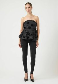 Czarny bezramkowy top z teksturowanej tkaniny, ozdobiony materiałowymi różami, z peplum i warstwowymi falbanami, w komplecie z czarnymi legginsami i szpilkami.