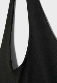 Gros plan d'un vêtement noir sans manches avec une large bretelle et un décolleté arrondi sur fond clair.