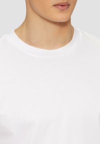 Weißes Baumwoll-T-Shirt mit rundem Halsausschnitt und kurzen Ärmeln. Glatte Textur und schlichtes Design ohne sichtbare Logos oder Muster.