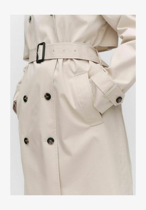 Beżowy płaszcz trench z podwójnymi guzikami, paskiem w talii i dwoma kieszeniami po bokach. Gładka tekstura i dopasowany krój.