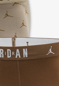 Δύο ζευγάρια αθλητικών σορτς: ένα μπεζ με χρυσά λογότυπα Jumpman και ένα καφέ με λευκή μέση με λογότυπο. Μαλακό ύφασμα και εφαρμοστή σχεδίαση.