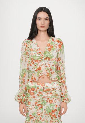 Floral crop top made of sheer fabric with button detail and puffy sleeves. Features orange and green floral patterns; paired with matching skirt.