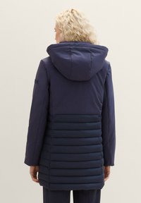 Granatowa kurtka puchowa z kapturem, z gładką tkaniną na górze oraz pikowanymi, ocieplonymi segmentami na dole.