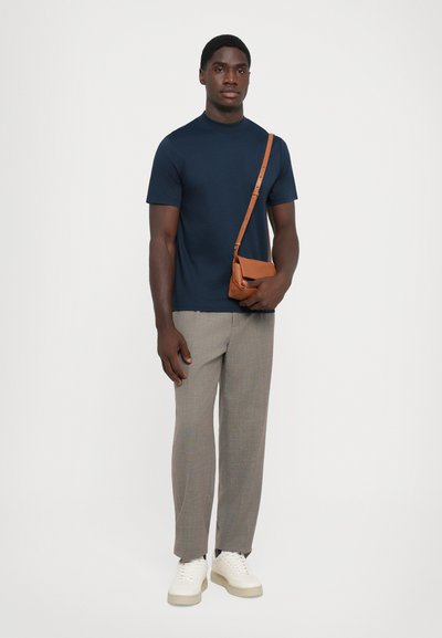 Cămașă bleumarin cu mâneci scurte, pantaloni în carouri gri deschis, adidași albi și o geantă de umăr maro. Ansamblu casual cu un design minimalist.