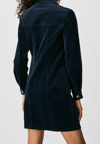 Mörkblå kord kjolklänning med långa ärmar, en knappmanchett och en rak skärning som faller ovanför knät, med en texturerad tygfinish.