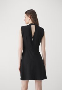 Black sleeveless dress with a high neck, cut-out back, and a zipper detail at the neckline. Smooth fabric with a fitted silhouette.