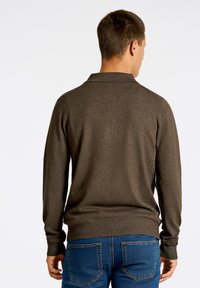 Brun långärmad pikétröja med stickad textur och krage, i kombination med blå denimjeans. Har ribbad nederkant och ärmslut.