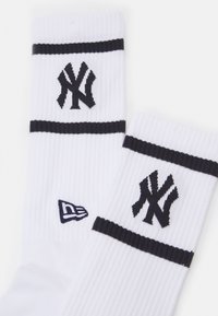 Calcetines blancos con textura de canalé, adornados con rayas negras y el logo de los New York Yankees en negro. Logo lateral: New Era.