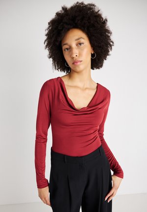 Bodysuit bordeaux à manches longues avec un col drapé et des détails froncés ; porté avec un pantalon noir taille haute. Texture lisse, design ajusté.