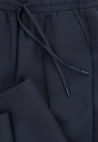 Marineblauwe joggerbroeken gemaakt van gladde stof, met zijzakken en een ontspannen pasvorm. De tailleband is elastisch voor verstelbaar comfort.