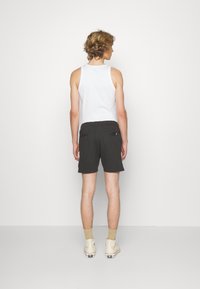 Zwarte shorts met een relaxed fit, twee achterzakken en een zachte textuur, gecombineerd met een witte tanktop en beige hoge sneakers.