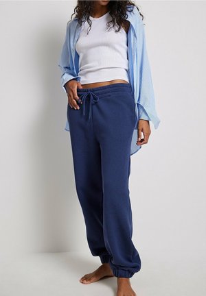 Marineblauwe joggingbroek met elastische boorden en een trekkoord in de taille, gecombineerd met een lichtblauw gestreept shirt over een witte tanktop.