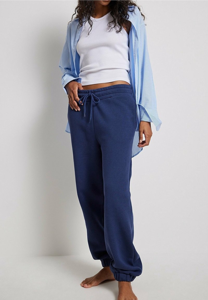 Marinblå träningsbyxor med elastiska muddar och snörning i midjan, kombinerat med en ljusblå randig skjorta över en vit linne.