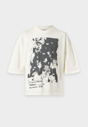 Un mannequin masculin porte un T-shirt blanc oversize à motif graphique et un pantalon gris foncé sur un fond clair uni.