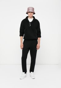 Black fleece pullover with a high collar, black sweatpants, white sneakers, and a light pink bucket hat. Sunglasses worn on the shirt.