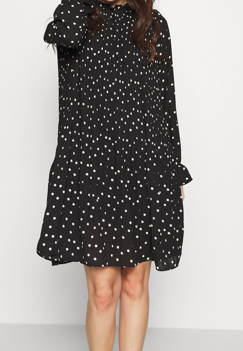 Svart klänning med långa ärmar, löst snitt och rynkad halsringning, prydd med vita prickar över hela tyget.