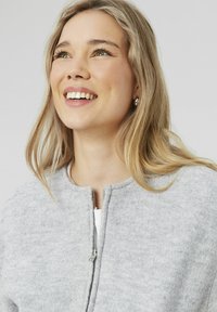 Veste zippée gris clair avec un col rond, fabriquée en tissu doux ; elle présente une fermeture éclair métallique et une surface texturée.