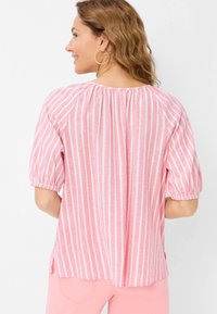 Rosa gestreifte Bluse mit Puffärmeln und gerafftem Ausschnitt. Der Stoff wirkt leicht und hat eine lockere Passform mit Seitenschlitzen.