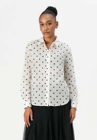 White button-up shirt made of sheer fabric with black polka dots, long sleeves, and a classic collar; unstructured fit.