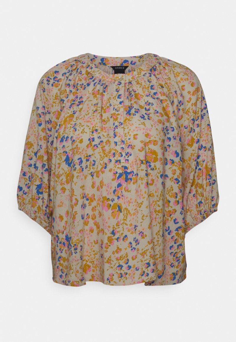 Blouse ample avec encolure ronde et manches 3/4, présentant un motif floral multicolore rose, bleu et moutarde sur fond beige.