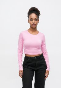 Langermet kort topp i myk rosa bomull, rund hals, smal passform, kombinert med høytlivs svarte bukser. Glatt tekstur, uten synlige mønstre.