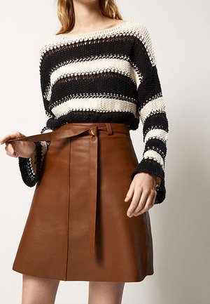 Woman wearing black and white striped knit sweater with wide sleeves and brown leather A-line skirt, adjusting skirt belt.