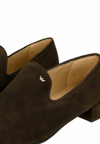 Para ciemnobrązowych zamszowych butów wsuwanych na niskim obcasie typu blok z beżową skórzaną wyściółką wewnętrzną, z małym metalowym logo na cholewce.