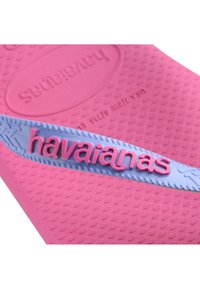 Rožinės guminės šlepetės su mėlynu dirželiu, ant kurio yra iškilus rožinis "havaianas" prekės ženklas. Tekstūruotas padas su raštuota apačia, užtikrinančia sukibimą.