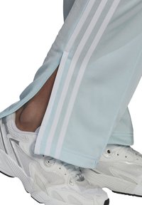 Lichtblauwe sportbroeken met witte zijstrepen, met een tapered ontwerp en splitten bij de enkels, gecombineerd met witte sneakers.