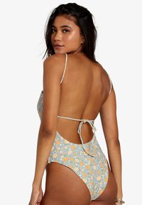 One-piece swimsuit with a light blue floral pattern, adjustable thin straps, open back design, and tie detail at the back.