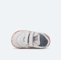 Zapatilla blanca con dos tiras de Velcro, cuero texturizado, suela de goma moteada y colorida, y forro de malla. Acentos reflectantes en los laterales.